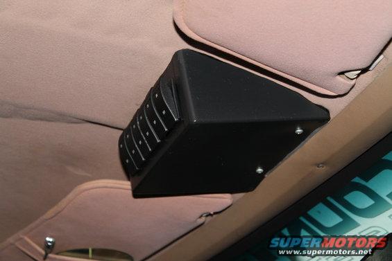 Black overhead console with multiple buttons mounted to the tan headliner of a vehicle