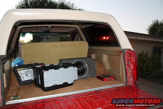 Interior of a red pickup truck bed with a subwoofer and toolboxes