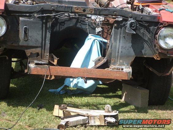 Rusty front end of a red vehicle under construction, showing exposed engine bay and frame