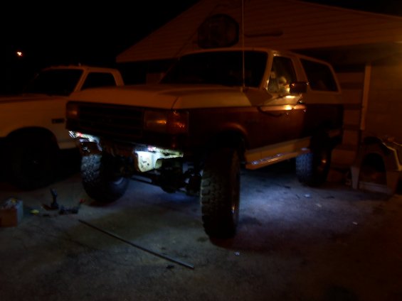 Two-tone brown and tan Ford Bronco with lifted suspension and aftermarket wheels, parked in a driveway at night