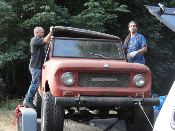 Two men working on a red International Scout on a trailer. The roof is open