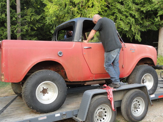 Red International Scout on a trailer, side view, with a man standing on the trailer next to it
