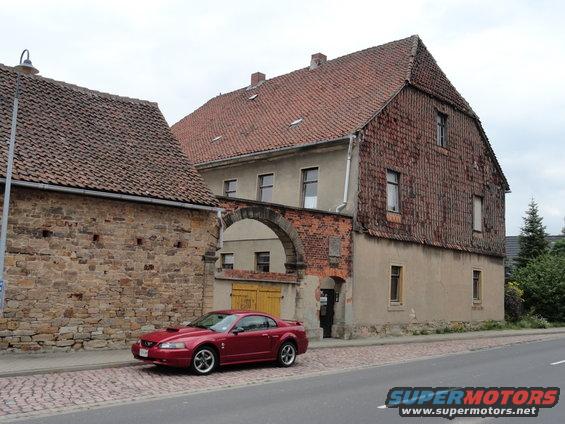 Red Ford Mustang parked on cobblestone street in front of old buildings