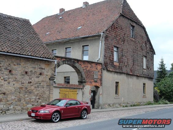 Red coupe parked on cobblestone street in front of old buildings