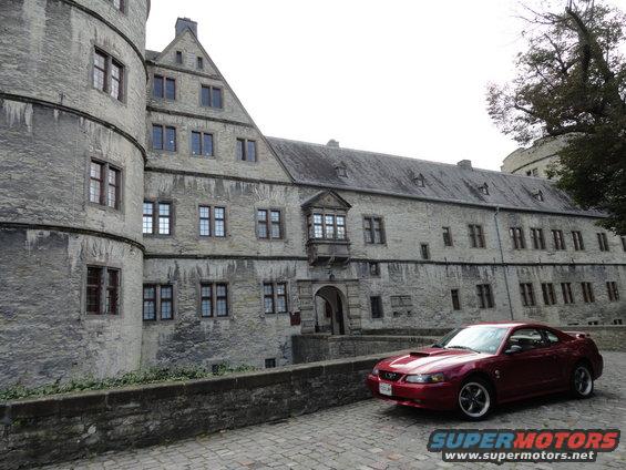 Red coupe parked on cobblestone in front of a stone building