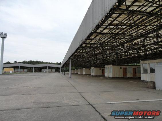 Large covered area with rows of small buildings, concrete lot, and a tall light pole