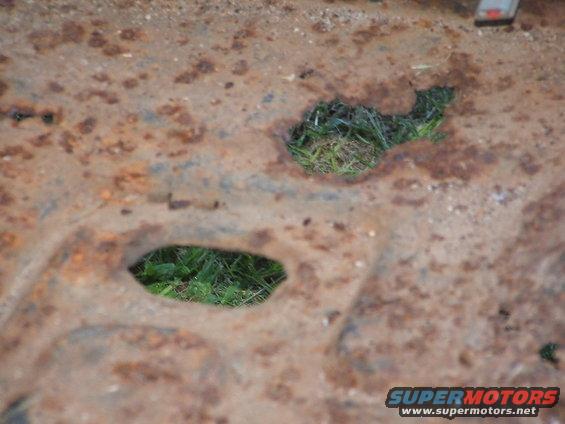 rusted metal panel with two holes showing grass underneath