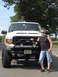 2001 Ford Excursion - A man poses next to a lifted white 2001 Ford Excursion with a custom front bumper and auxiliary lights.