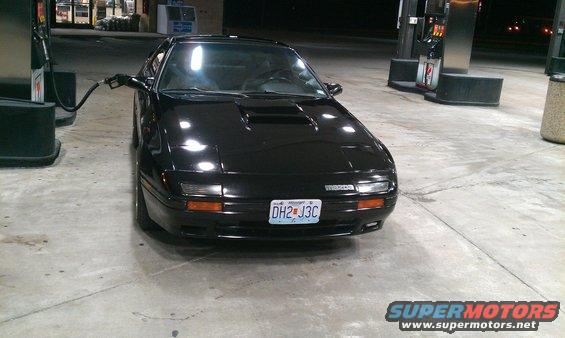 Black 1988 Mazda RX-7 with a hood scoop at a gas pump