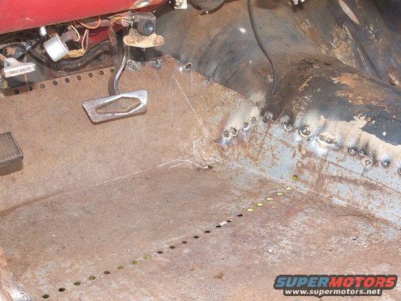 Rusted interior floor pan with brake and gas pedals, wiring, and visible welds
