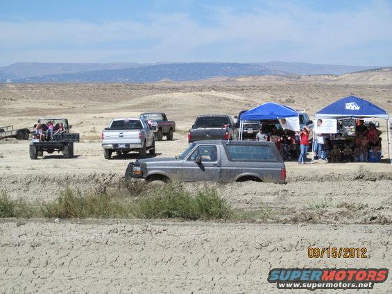 Gray SUV stuck in mud with other vehicles and tents in background