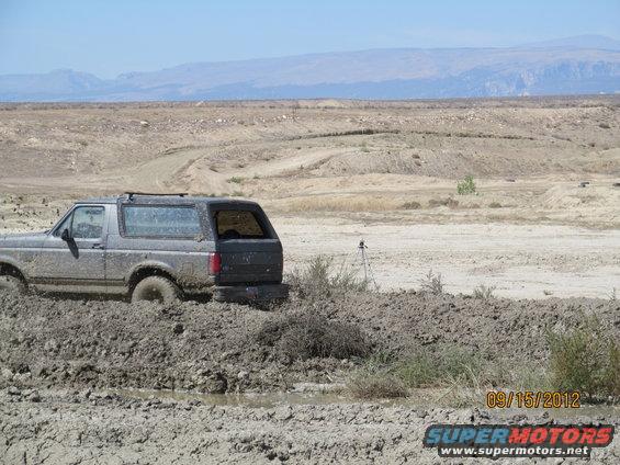 Mud-covered Ford Bronco stuck in a muddy field. Mountains in background