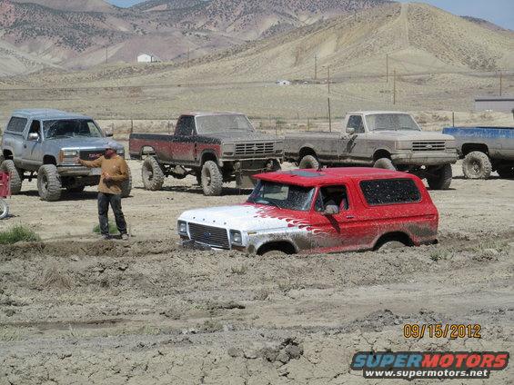 Red and white Ford Bronco with flame decals stuck in mud, front grille visible