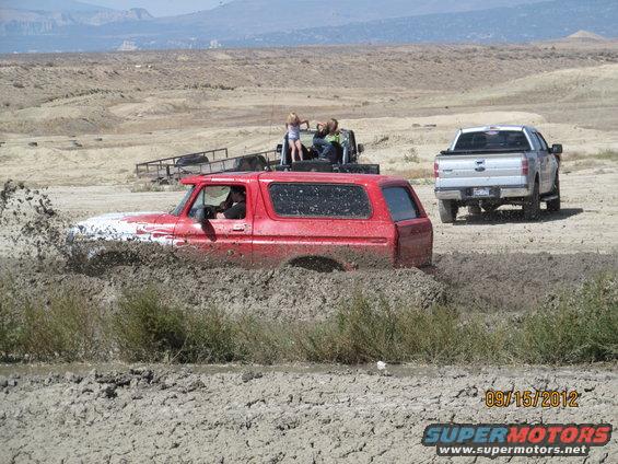 Red SUV stuck in mud, with a silver pickup truck in the background