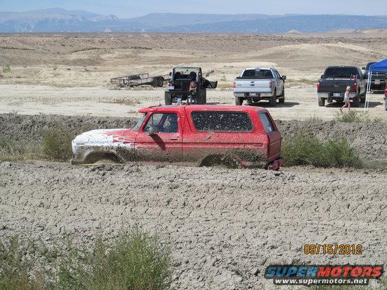 Red SUV stuck in mud, front half submerged, white paint on hood