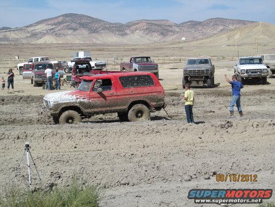 red 1979 Ford Bronco stuck in mud with people around and other trucks in background