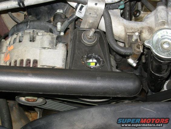 altl14.jpg This is fully installed & working, with the engine idling.  Considering how the previous belt appeared to have stretched, I intentionally set my idler pulley so the tensioner is close to its "new belt" limit.  Whether this one stretches or not, it fits & works.  But if it does stretch, it has a long way to go before the tensioner bottoms out.

After hole-sawing through that tab, I discovered it's hollow, and is part of the reservoir cavity.  That's why I had to glue the patch around the hole to seal the edge.  But it still makes more sense than having the tensioner gauge covered.