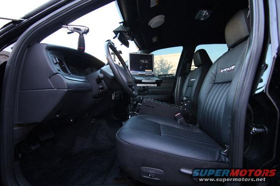 Black leather police car interior with laptop displaying "POLICE", steering wheel, and shotgun mount