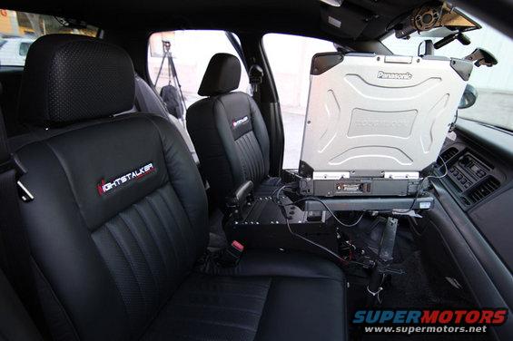 Interior view of a 2004 Ford Crown Victoria police car showing front seats, dashboard, and a Panasonic laptop mounted between the seats