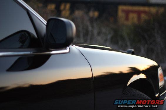 Close-up of black sedan's fender and side mirror with sunset reflection