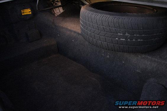 trunk interior with spare tire and a yellow warning sticker