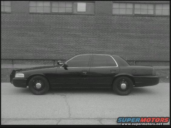Black 2004 Ford Crown Victoria police car, side view, parked on pavement in front of brick building