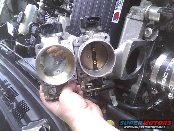 Hand holding a throttle body next to another installed throttle body in an engine bay