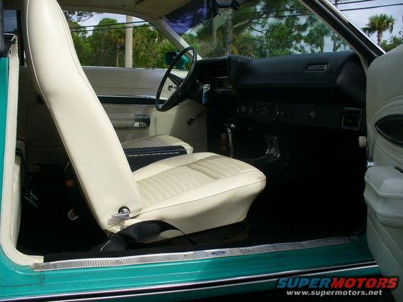 Interior shot of a teal car with white seats and black dashboard. Steering wheel and door panel visible