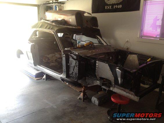 Car body on jack stands, doors off, engine bay open. Parts stacked on roof. Garage setting
