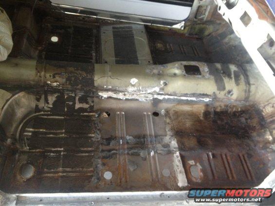 Car interior floor pan showing rust and repair work, viewed from above