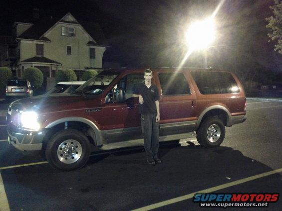 Red Ford Excursion parked at night, person standing by driver's door