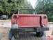 1961 International Scout 80 - This red pickup truck, possibly an International Scout, is seen from the rear on a trailer with a flatbed truck in the distance.