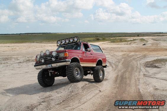 Red lifted Ford Bronco with roof lights and extra fog lights on a dirt track