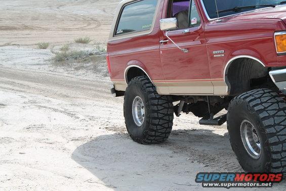 Red Ford Bronco with tan trim, lifted with large tires, on a dirt road