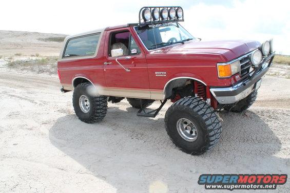 1990 Ford Bronco modified for off-roading, parked on sandy terrain with large tires and a light bar