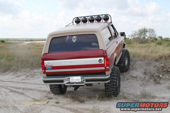 1990 Ford Bronco with off-road tires and roof lights on a dirt hill