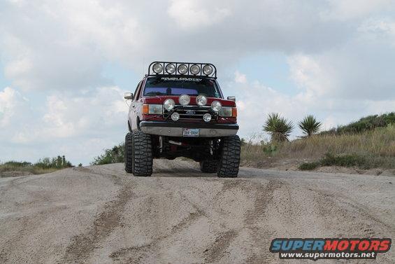 1990 Ford Bronco lifted with off-road lights on a dirt hill