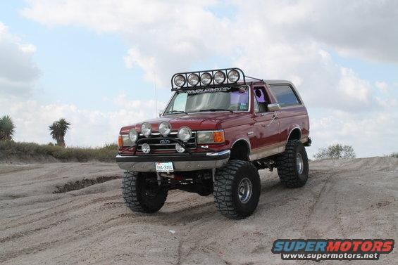 Red Ford Bronco with off-road modifications on a dirt track