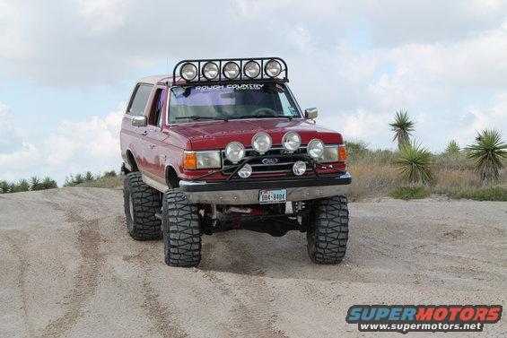 Red 1990 Ford Bronco with lift kit and extra lights on a dirt road
