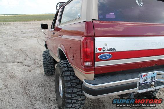 Red 1990 Ford Bronco with lifted suspension and large tires, viewed from the rear quarter