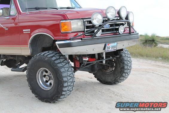 Lifted red Ford truck with off-road lights and big tires, parked on a dirt road