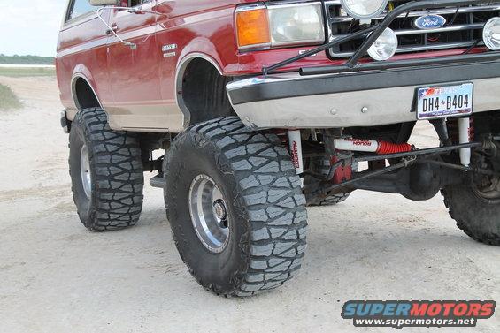 Red Ford Bronco with tan lower body panels and large off-road tires, viewed from the front 3/4 angle