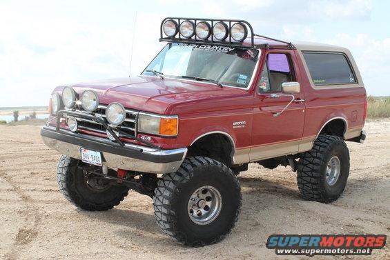 Red lifted 1990 Ford Bronco with roof-mounted lights and brush guard