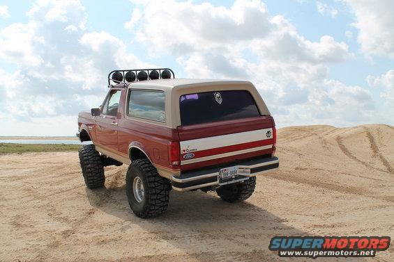 Red and tan Ford Bronco with off-road tires and light bar, parked on sand dunes
