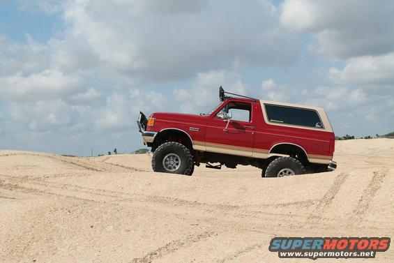 1990 Ford Bronco with lifted suspension and off-road tires driving through sand dunes