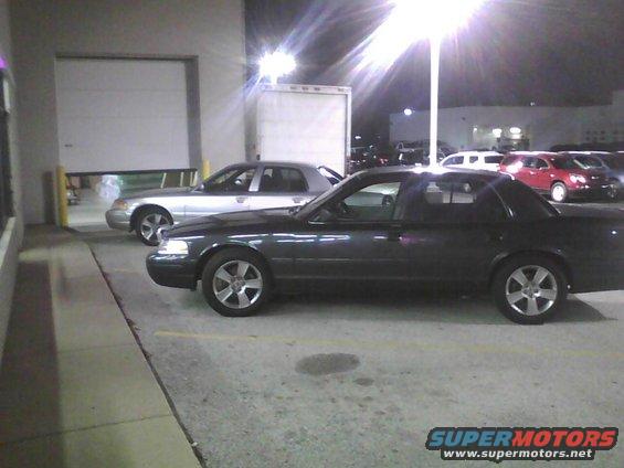 Dark 2003 Ford Crown Victoria side view, parked next to a silver sedan
