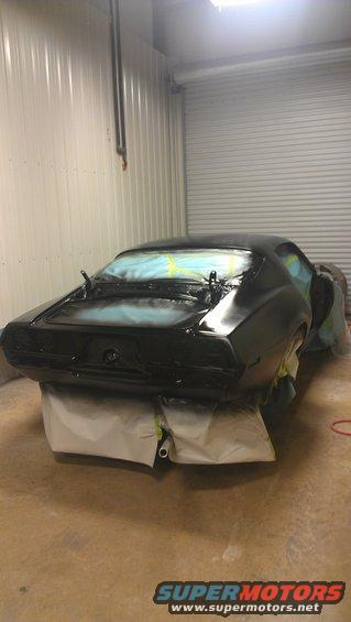 1973 Chevrolet Camaro rear end covered in black primer, masked for painting in a spray booth