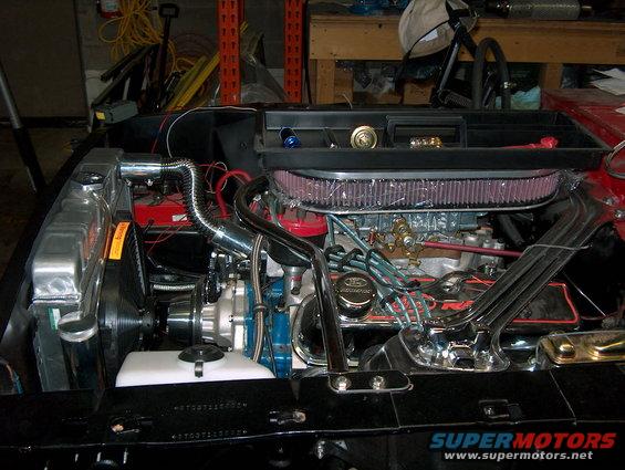 Engine bay with V8 engine, chrome details, and air filter. Supermotors.net logo visible