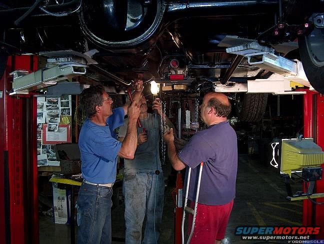 Three men working on the underside of a vehicle raised on a lift in a garage
