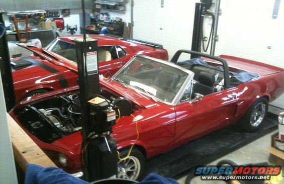 Red convertible with black interior and roll bar, hood open, in garage